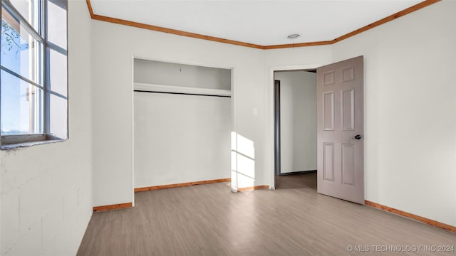 unfurnished bedroom with a closet, light hardwood / wood-style floors, multiple windows, and ornamental molding