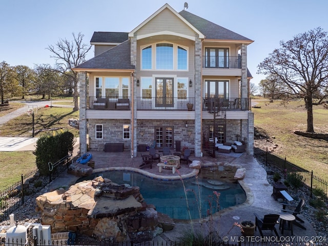 rear view of property featuring french doors, an outdoor fire pit, a balcony, a fenced in pool, and a patio