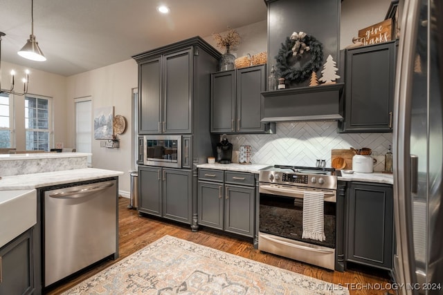 kitchen featuring hardwood / wood-style floors, backsplash, light stone countertops, decorative light fixtures, and stainless steel appliances