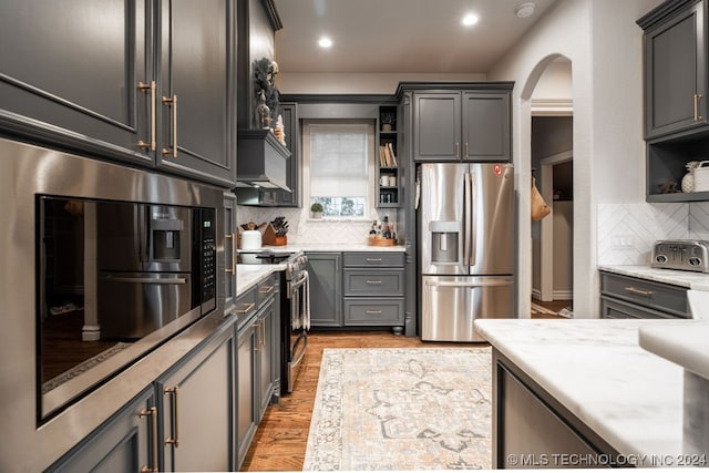 kitchen with appliances with stainless steel finishes, tasteful backsplash, light stone counters, gray cabinetry, and light hardwood / wood-style flooring