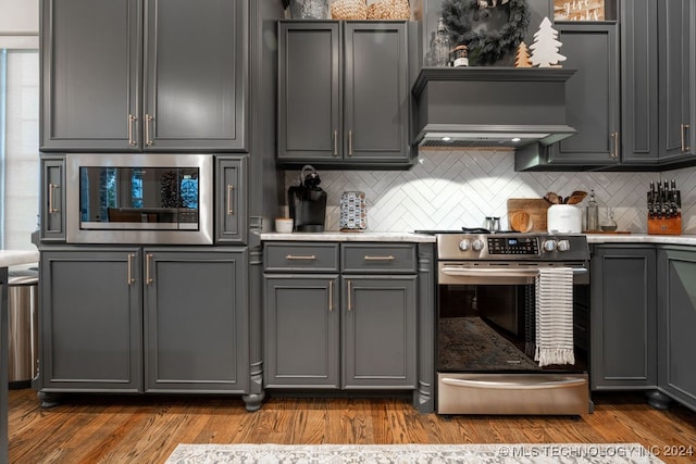 kitchen with appliances with stainless steel finishes, hardwood / wood-style flooring, gray cabinets, and tasteful backsplash