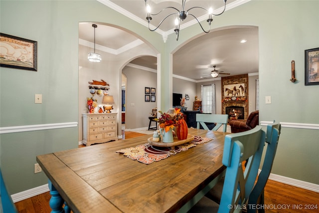 dining room with ceiling fan with notable chandelier, dark hardwood / wood-style flooring, a large fireplace, and crown molding