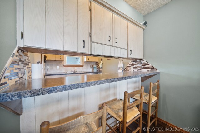 kitchen featuring a kitchen bar, decorative backsplash, light brown cabinets, and a textured ceiling