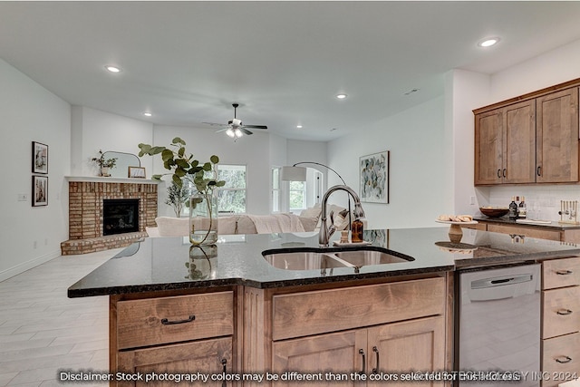 kitchen featuring a fireplace, dishwasher, dark stone counters, and sink