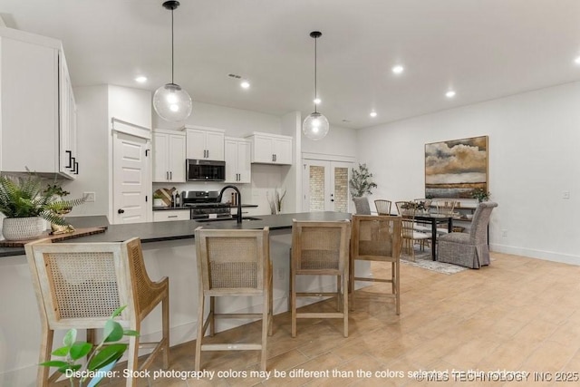 kitchen with white cabinets, appliances with stainless steel finishes, dark countertops, a kitchen bar, and decorative light fixtures