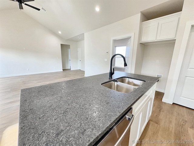 kitchen featuring lofted ceiling, a sink, white cabinets, stainless steel dishwasher, and dark stone countertops