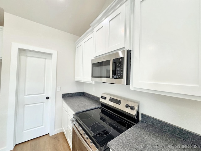 kitchen with appliances with stainless steel finishes, dark countertops, light wood-type flooring, and white cabinets