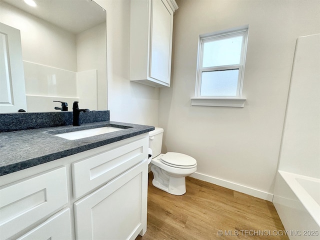 full bathroom featuring toilet, wood finished floors, vanity, baseboards, and a bath