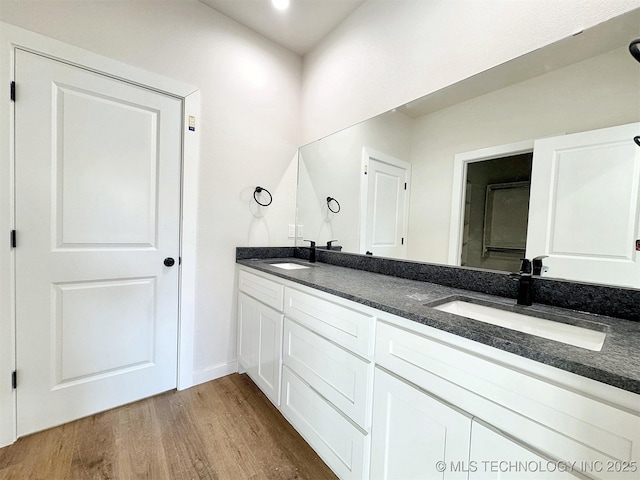 full bathroom featuring double vanity, wood finished floors, a sink, and baseboards