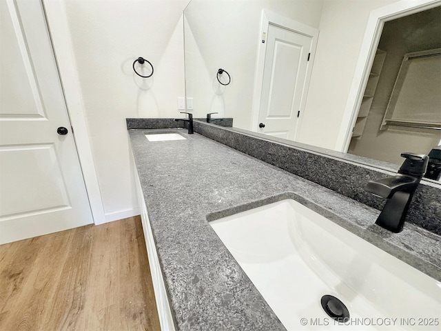 bathroom with double vanity, baseboards, a sink, and wood finished floors