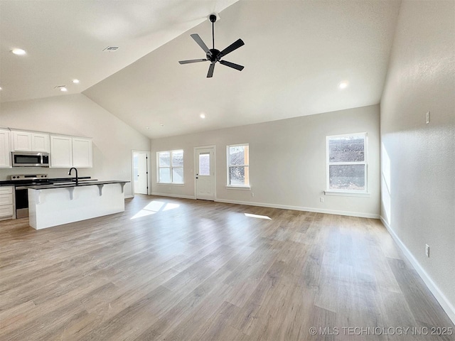 890 E Harlan Dr, Tahlequah, OK 74464 - unfurnished living room featuring baseboards, high vaulted ceiling, light wood-style floors, and a sink