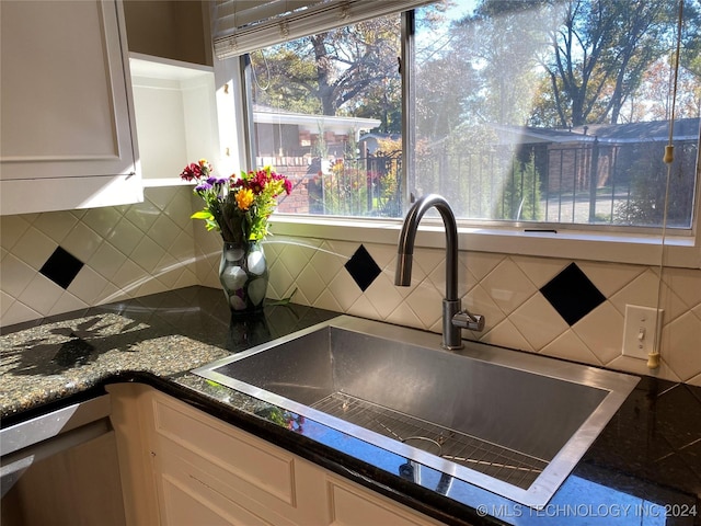 kitchen with tasteful backsplash, stainless steel dishwasher, sink, dark stone countertops, and white cabinetry