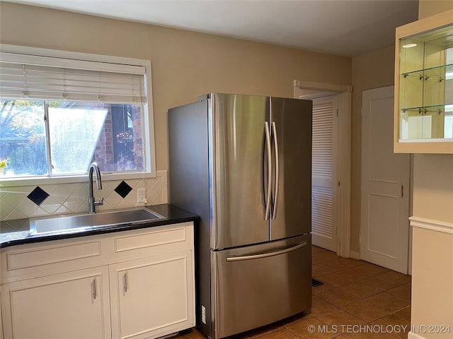 kitchen with stainless steel fridge, tasteful backsplash, sink, tile patterned flooring, and white cabinetry