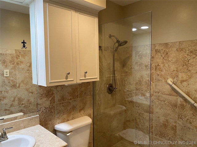 bathroom featuring toilet, a tile shower, tile walls, and vanity