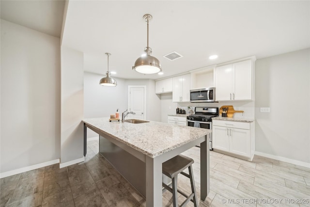 kitchen with sink, stainless steel appliances, decorative light fixtures, a breakfast bar area, and white cabinets