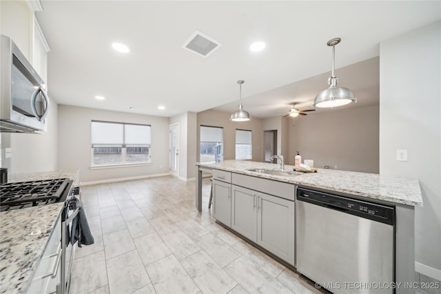 kitchen with pendant lighting, sink, ceiling fan, light stone countertops, and appliances with stainless steel finishes