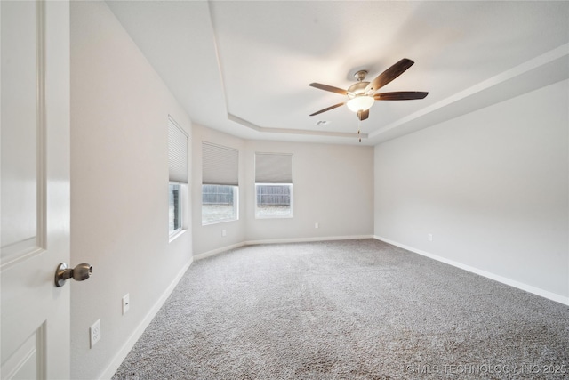 spare room featuring a raised ceiling, ceiling fan, and carpet