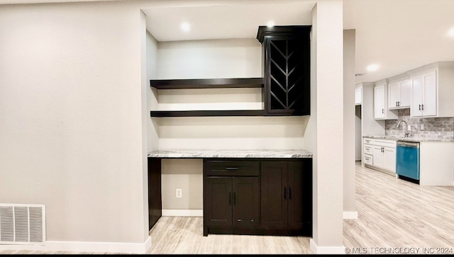 interior space featuring dishwasher, tasteful backsplash, light stone counters, light hardwood / wood-style flooring, and white cabinets