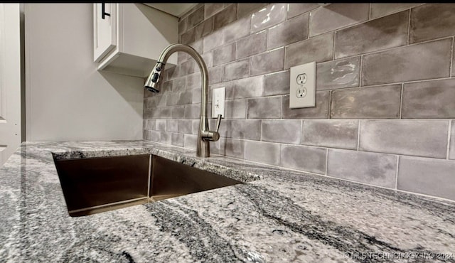 room details featuring white cabinetry, sink, and stone countertops