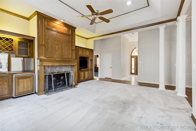 unfurnished living room featuring a raised ceiling, ornate columns, crown molding, and ceiling fan