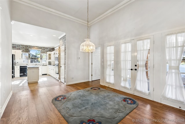 foyer entrance featuring an inviting chandelier, french doors, crown molding, and light hardwood / wood-style flooring