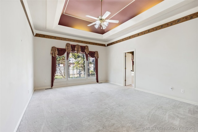 unfurnished room featuring a tray ceiling, ceiling fan, crown molding, and light colored carpet