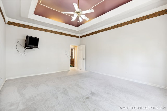 carpeted empty room with a raised ceiling, ceiling fan, and crown molding