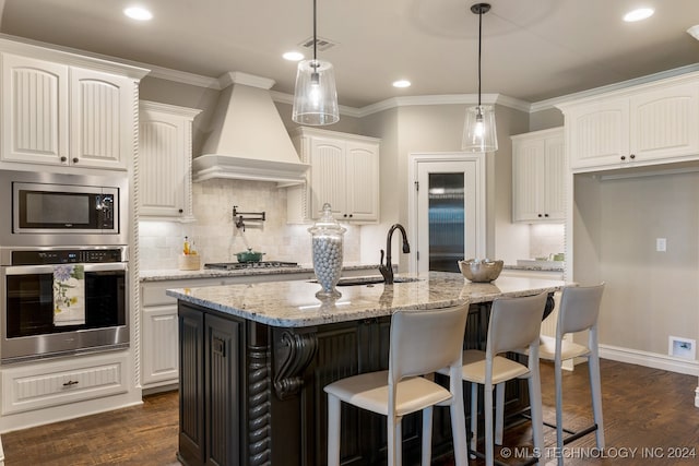 kitchen with premium range hood, white cabinets, a center island with sink, light stone countertops, and stainless steel appliances