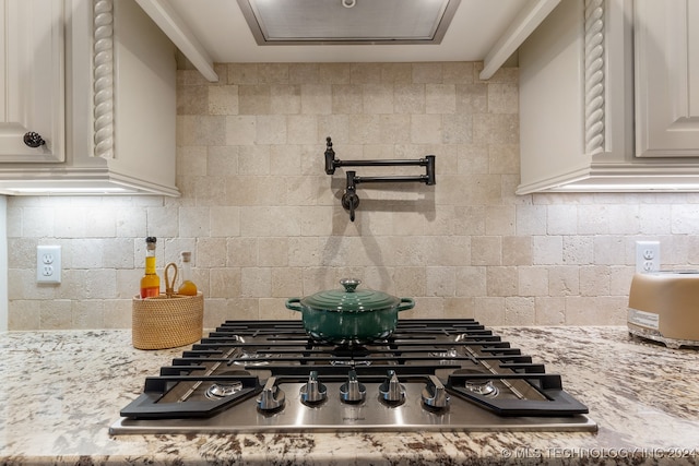 kitchen with backsplash, light stone counters, white cabinetry, and stainless steel gas cooktop