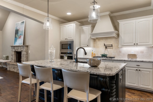 kitchen featuring premium range hood, a center island with sink, appliances with stainless steel finishes, dark hardwood / wood-style flooring, and white cabinetry