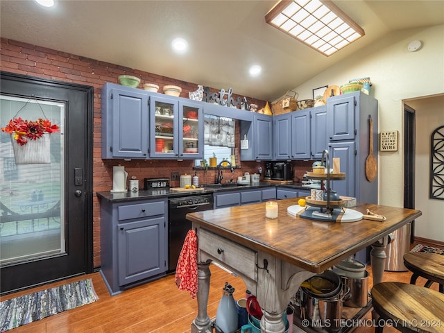 kitchen featuring dishwasher, sink, light hardwood / wood-style flooring, vaulted ceiling, and brick wall