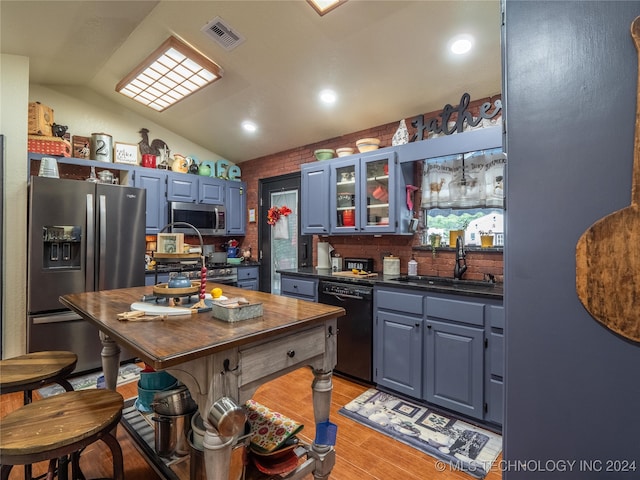 kitchen featuring sink, blue cabinets, light hardwood / wood-style floors, vaulted ceiling, and appliances with stainless steel finishes