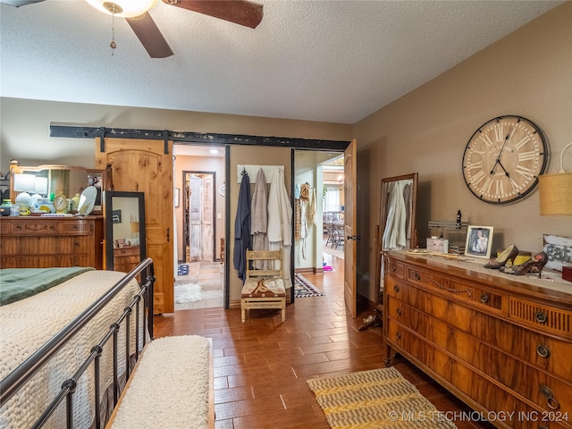 bedroom featuring a barn door, ceiling fan, dark hardwood / wood-style flooring, and a textured ceiling