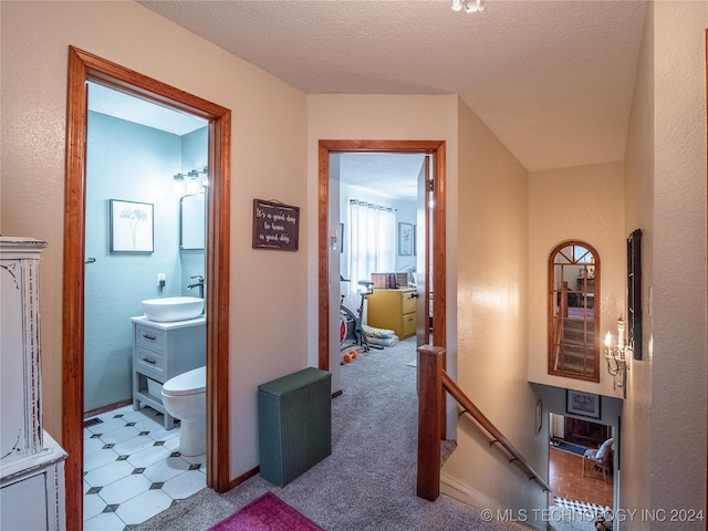 corridor with light carpet, sink, and a textured ceiling