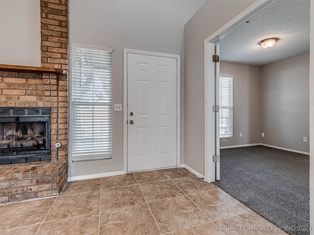 carpeted entrance foyer featuring a textured ceiling and a brick fireplace