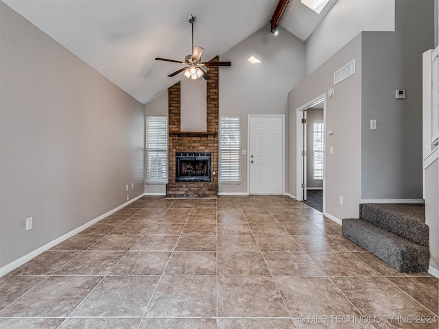 unfurnished living room featuring beam ceiling, a skylight, ceiling fan, a brick fireplace, and high vaulted ceiling