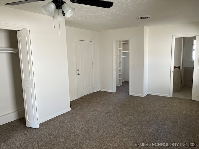 unfurnished bedroom featuring dark colored carpet, a textured ceiling, ensuite bath, and ceiling fan