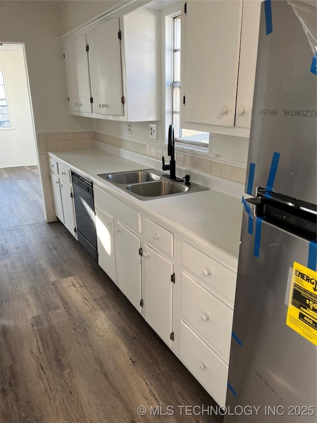 kitchen with black dishwasher, a sink, freestanding refrigerator, and white cabinetry