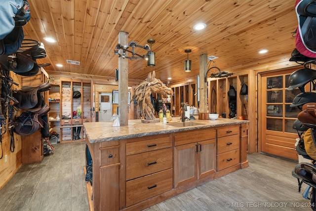 kitchen featuring a kitchen island with sink, wood walls, sink, and light hardwood / wood-style floors