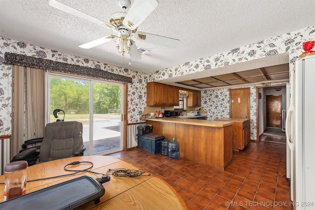 kitchen with kitchen peninsula, ceiling fan, dark tile patterned floors, and a textured ceiling