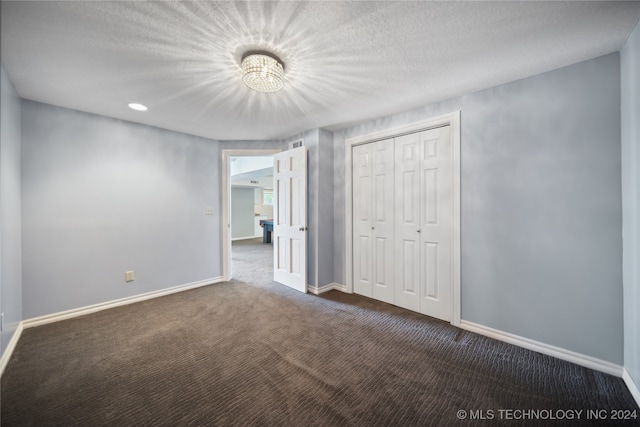 unfurnished bedroom with a closet, dark carpet, and a textured ceiling