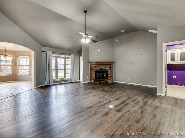 unfurnished living room with a brick fireplace, ceiling fan with notable chandelier, vaulted ceiling, and hardwood / wood-style flooring