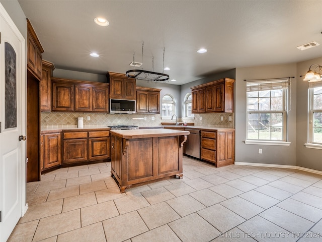 kitchen with appliances with stainless steel finishes, backsplash, a kitchen island, and a healthy amount of sunlight