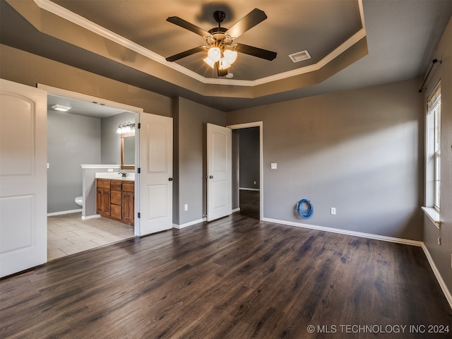 unfurnished bedroom featuring ensuite bath, ornamental molding, a tray ceiling, ceiling fan, and hardwood / wood-style flooring