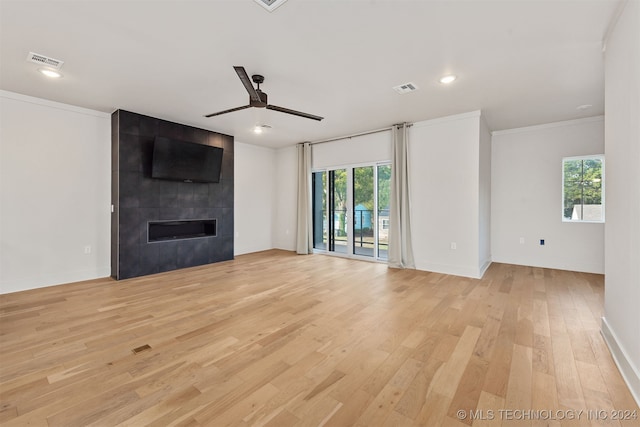 unfurnished living room featuring crown molding, a fireplace, a wealth of natural light, and light hardwood / wood-style flooring