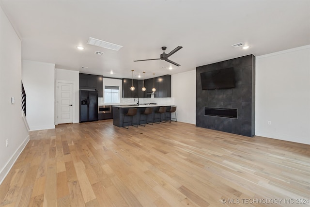 unfurnished living room with light wood-type flooring, ornamental molding, ceiling fan, sink, and a fireplace