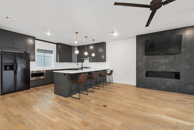 kitchen featuring stainless steel microwave, a kitchen breakfast bar, black refrigerator with ice dispenser, light hardwood / wood-style floors, and decorative light fixtures