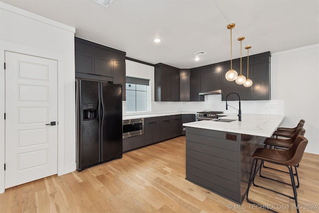 kitchen with kitchen peninsula, appliances with stainless steel finishes, sink, decorative light fixtures, and light hardwood / wood-style flooring