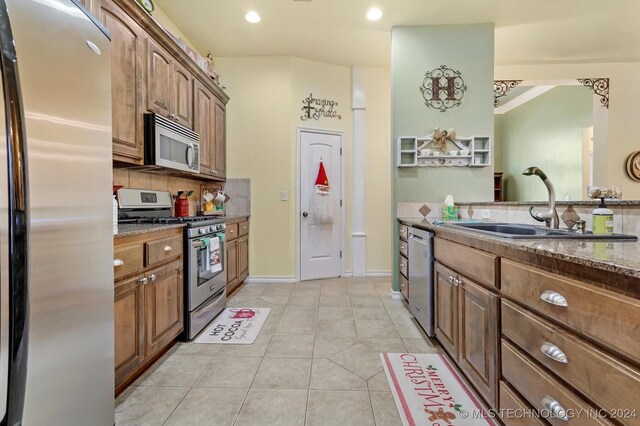 kitchen featuring light tile patterned flooring, sink, appliances with stainless steel finishes, dark stone counters, and decorative backsplash