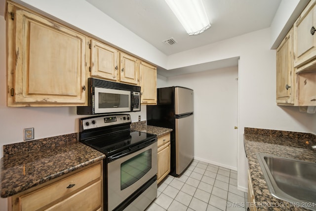 kitchen featuring dark stone counters, sink, light tile patterned floors, light brown cabinetry, and appliances with stainless steel finishes